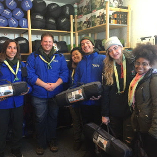 Group of people in blue jackets with slepping bags and tents in a store setting