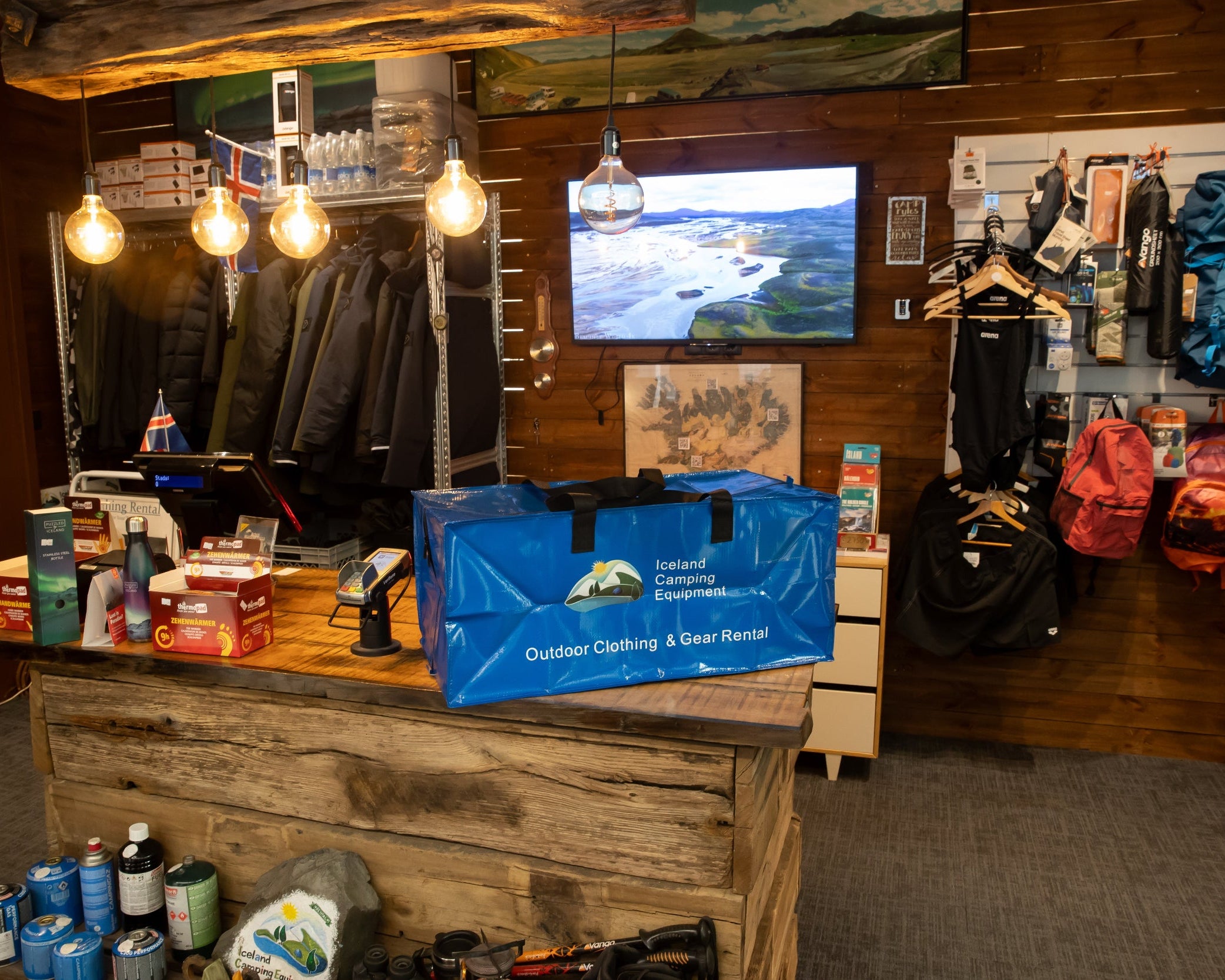 Indoor setting with outdoor gear and clothing display, including a TV screen showing a scenic landscape.